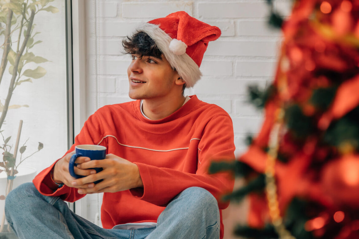 Un adolescent souriant tenant un cadeau de Noël près du sapin, entouré de décorations festives et d'une ambiance chaleureuse